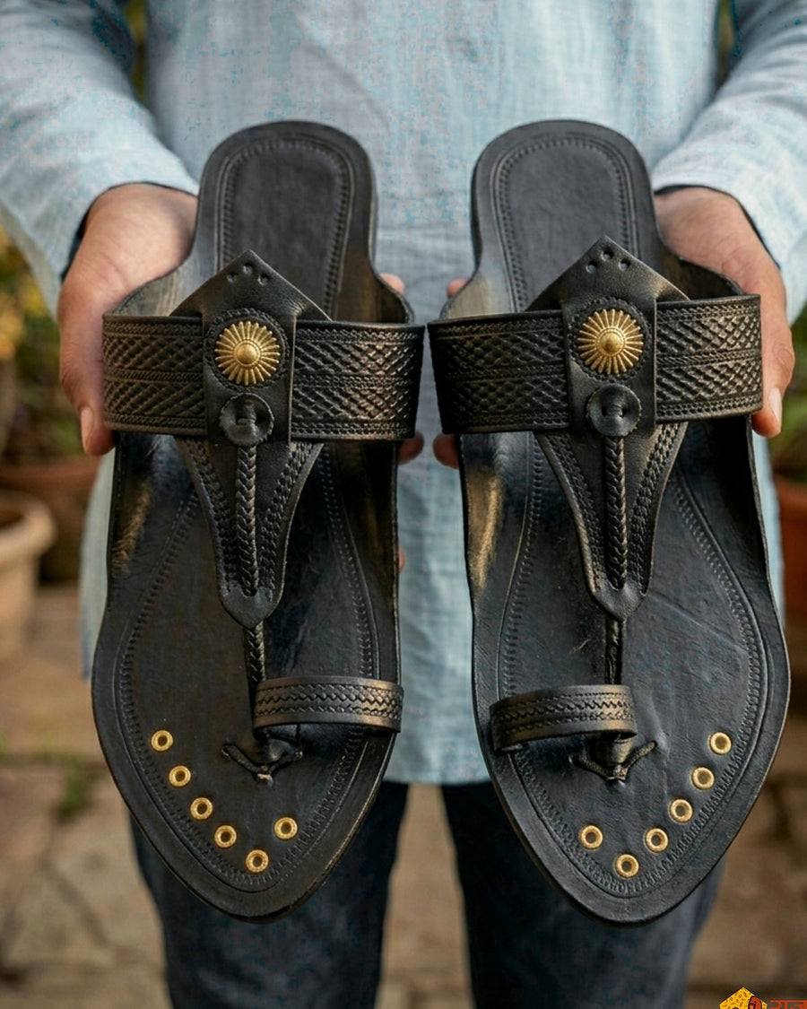 Kolhapur Original in black, a pair held up in an artisan's hands