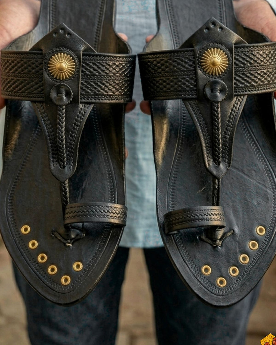 Kolhapur Original in black, a pair held up in an artisan's hands